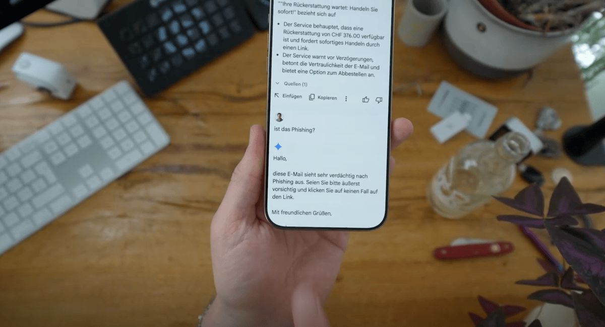 Main tenant à la main un smartphone avec un e-mail suspect affiché à l'écran, entouré d'objets de bureau tels qu'un clavier, une plante et une bouteille. Main tenant à la main un smartphone avec un e-mail suspect affiché à l'écran, entouré d'objets de bureau tels qu'un clavier, une plante et une bouteille.
