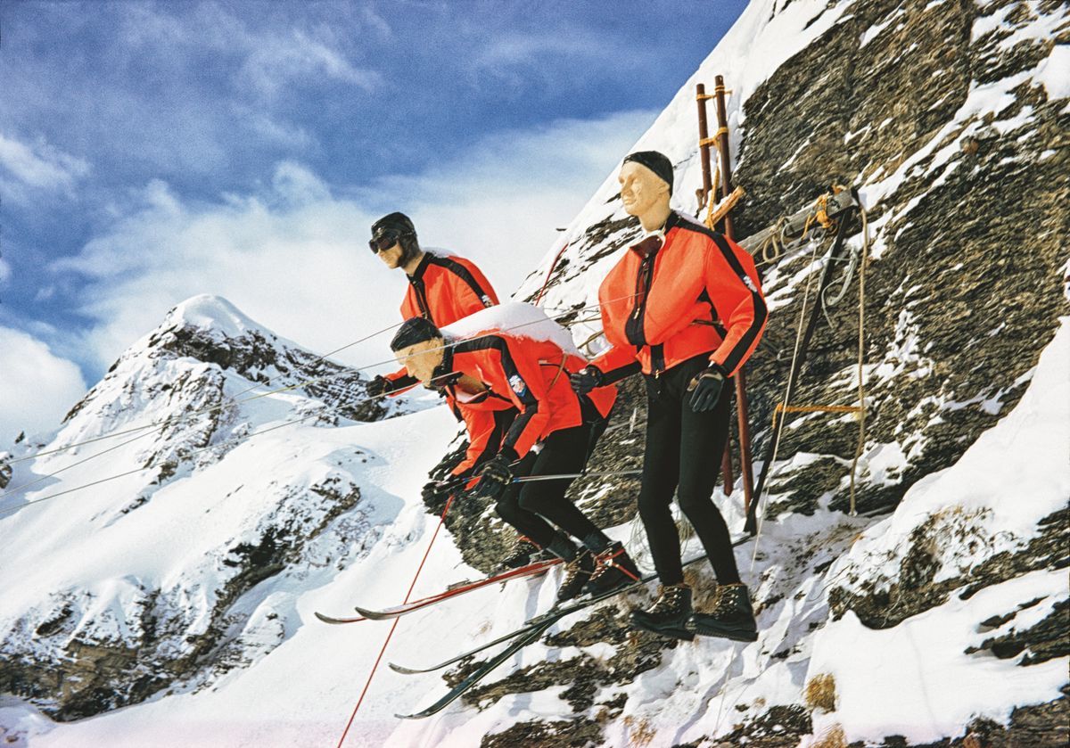 Trois skieurs en combinaisons rouges sur le point de descendre une pente enneigée, avec des montagnes en arrière-plan. Trois skieurs en combinaisons rouges sur le point de descendre une pente enneigée, avec des montagnes en arrière-plan.