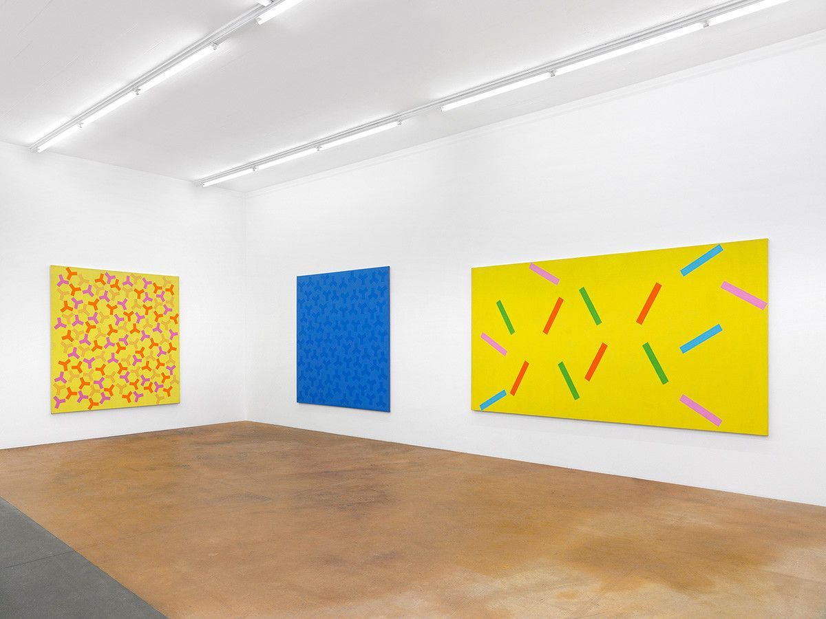 Galerie d'art moderne avec toiles colorées accrochées au mur blanc, y compris les œuvres jaunes avec des motifs de ligne et une toile bleue centrale. Galerie d'art moderne avec toiles colorées accrochées au mur blanc, y compris les œuvres jaunes avec des motifs de ligne et une toile bleue centrale.