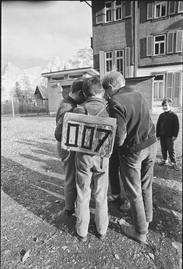 Les enfants se sont regroupés autour d'un panel marqué «007» dans une cour ensoleillée, avec des montagnes en arrière-plan. Les enfants se sont regroupés autour d'un panel marqué «007» dans une cour ensoleillée, avec des montagnes en arrière-plan.