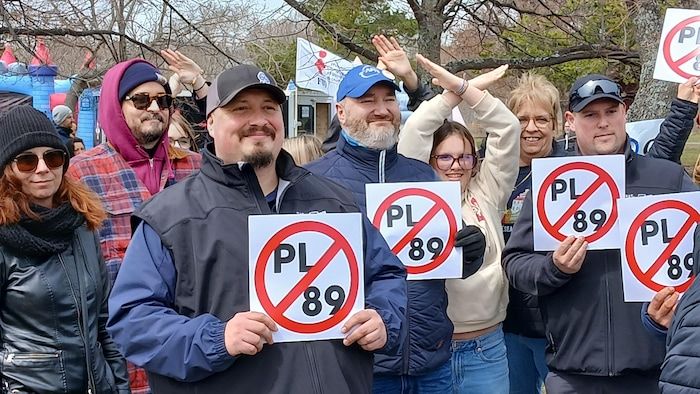 Un groupe de personnes proteste avec ses bras et ses signes interdisant le PL-89.