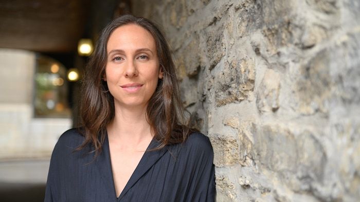 La femme, qui porte une chemise noire et se penche contre un mur de pierre, regarde le but.