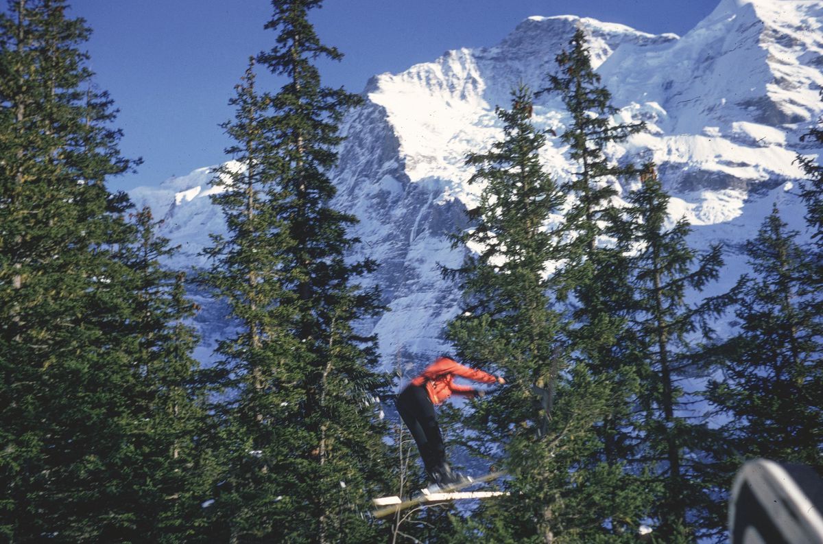 Skier en plein saut parmi les sapins, avec une montagne enneigée en arrière-plan. Skier en plein saut parmi les sapins, avec une montagne enneigée en arrière-plan.