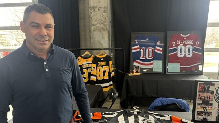 Un homme devant un kiosque où se trouvent des pulls de hockey.