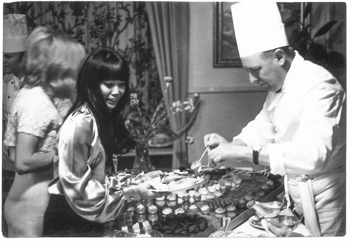 Un chef en vêtements blancs sert de la nourriture pour une femme souriante lors d'un élégant buffet. Un chef en vêtements blancs sert de la nourriture pour une femme souriante lors d'un élégant buffet.