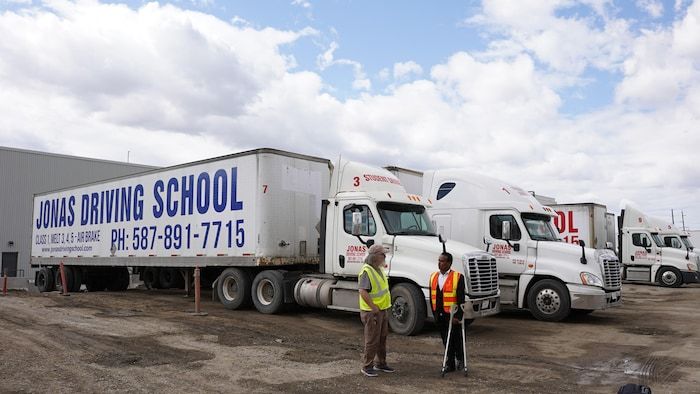 Jonas Hila, fondatrice de la Jonas Driving School Driving School, discutant avec un employé devant des camions de son école de conduite.