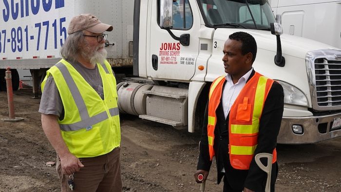 Jonas Hila, fondatrice de la Jonas Driving School Driving School, discute avec un homme devant un camion de remorque de son école.
